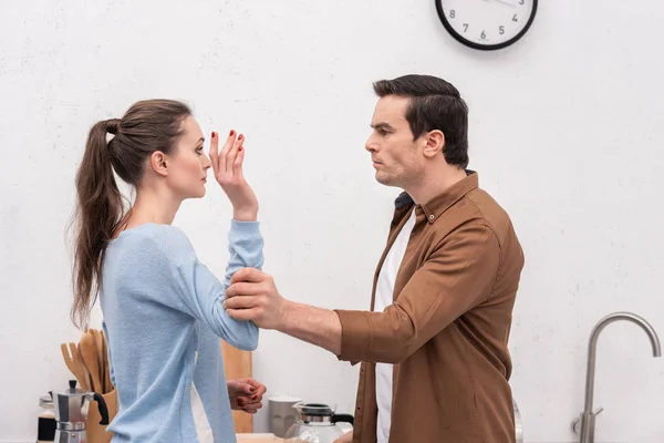 Loco hombre de la mano de la mujer durante la discusión en la cocina - foto de stock