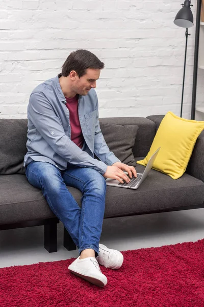 Handsome adult freelancer using laptop on couch at home — Stock Photo