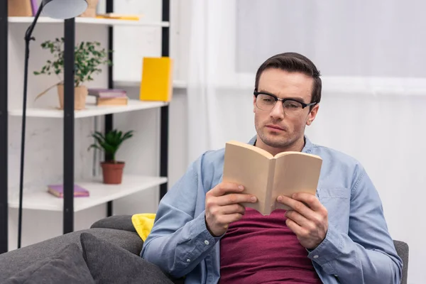 Концентрований дорослий чоловік читає книгу на дивані вдома — стокове фото