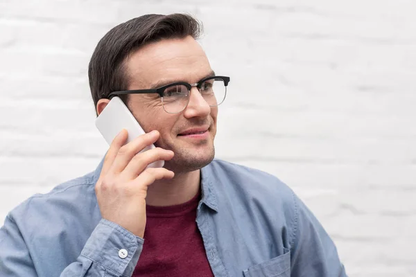 Close-up portrait of happy adult man talking by phone in front of white brick wall — Stock Photo