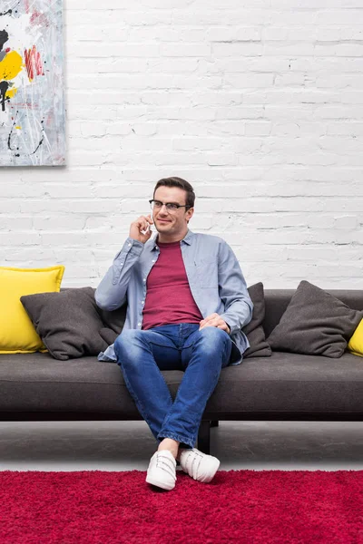 Sorrindo homem adulto falando por telefone no sofá em casa — Fotografia de Stock