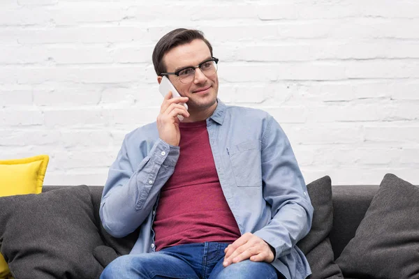 Счастливый взрослый мужчина разговаривает по телефону на диване дома — стоковое фото