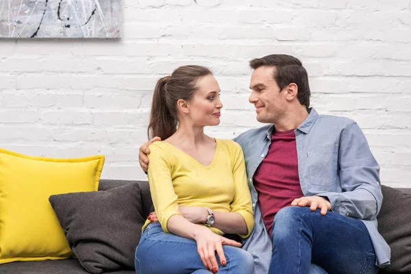 Beau couple adulte assis sur le canapé à la maison et se regardant joyeusement — Photo de stock