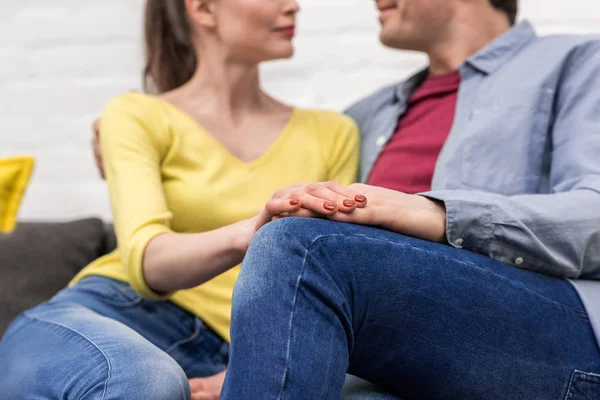 Abgeschnittene Aufnahme eines erwachsenen Paares, das Händchen hält, während es zu Hause auf der Couch sitzt — Stockfoto