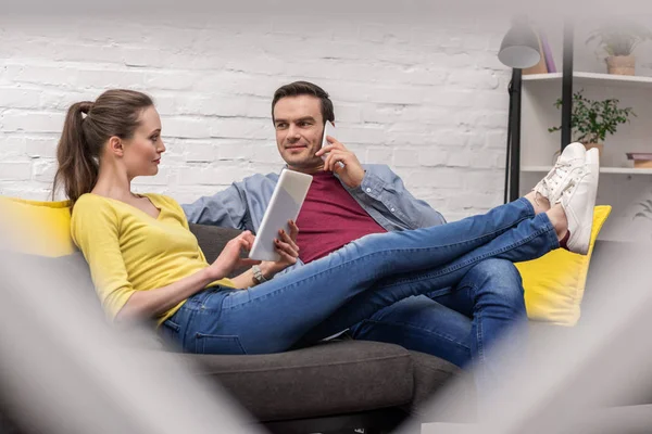 Sorrindo casal adulto relaxante no sofá em casa e usando gadgets — Fotografia de Stock