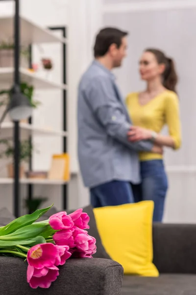 Bouquet of tulips lying on couch with beautiful adult couple embracing blurred on background — Stock Photo