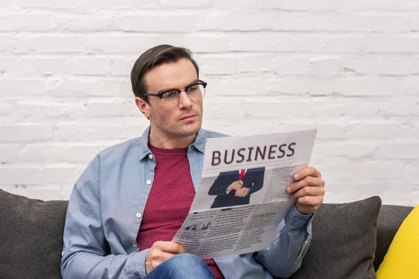 Konzentrierter erwachsener Mann liest zu Hause auf Couch Wirtschaftszeitung — Stockfoto