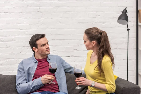 Belo casal adulto com copos de vinho tinto sentado no sofá em casa — Fotografia de Stock