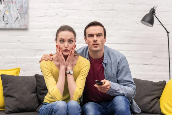 Schockiertes erwachsenes Paar vor dem Fernseher zusammen auf der Couch — Stockfoto