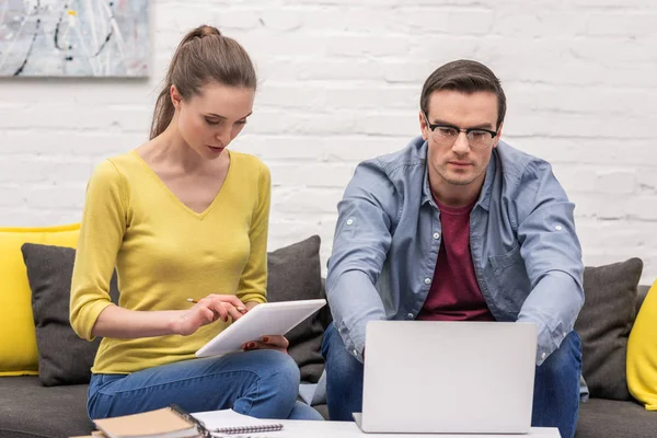 Pareja de freelancers adultos enfocados trabajando en el sofá en casa juntos - foto de stock