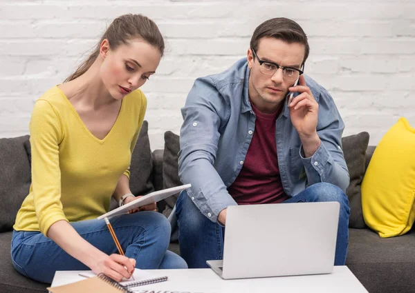 Couple adulte sérieux de pigistes travaillant sur le canapé à la maison ensemble — Photo de stock