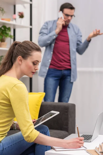 Erwachsene Frau arbeitet mit Tablet, während ihr Freund zu Hause telefoniert — Stockfoto