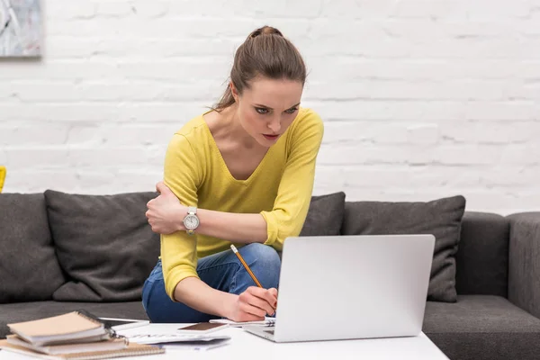 Serious adult woman working with laptop at home on couch — Stock Photo