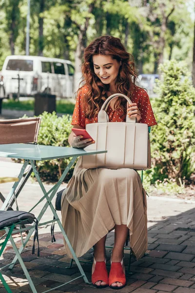 Mulher elegante com saco usando smartphone enquanto sentado no terraço no café — Fotografia de Stock