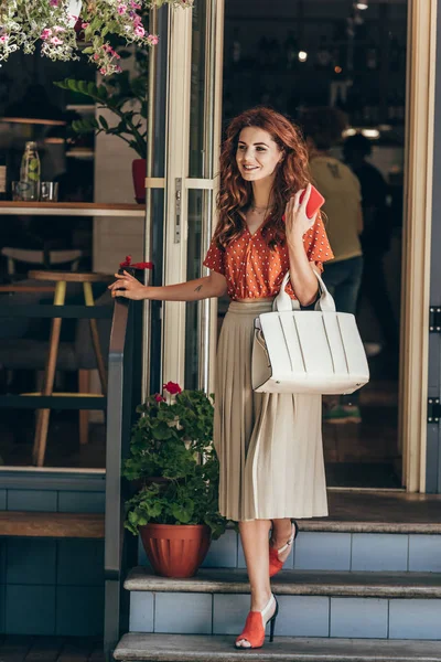 Mulher elegante com smartphone e saco saindo café — Fotografia de Stock