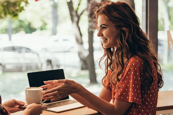 Vista parcial de la mujer sonriente tomando una taza de café de la camarera en la cafetería - foto de stock