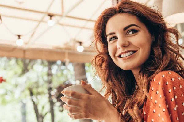 Vista lateral da mulher sorridente com xícara de café aromático no café — Fotografia de Stock