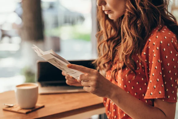 Частковий вид жінки читає газету за столом з ноутбуком в кав'ярні — стокове фото