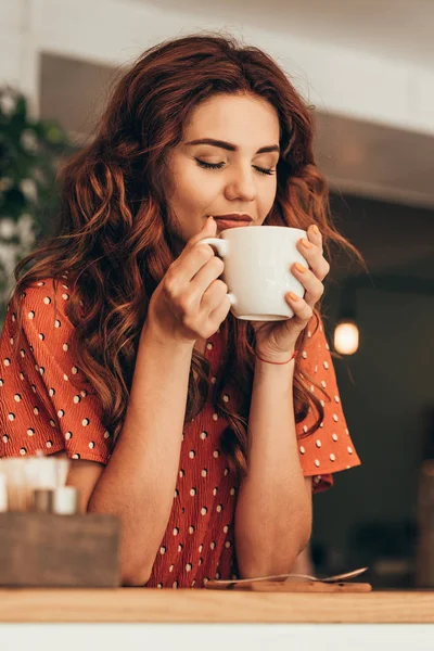 Portrait of beautiful woman with eye closed holding cup of aromatic coffee in hands in cafe — Stock Photo