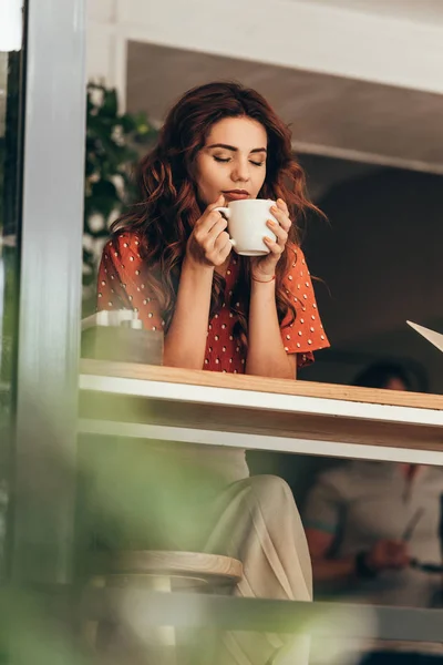 Retrato de mulher bonita com olho fechado segurando xícara de café aromático em mãos no café — Fotografia de Stock