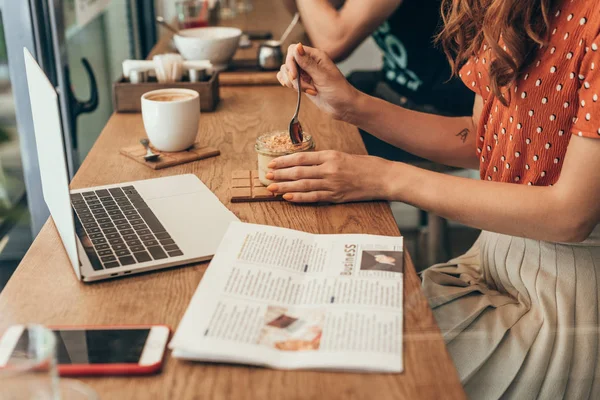 Vista parziale di donna che mangia soufflé a tavola con computer portatile in caffetteria — Foto stock