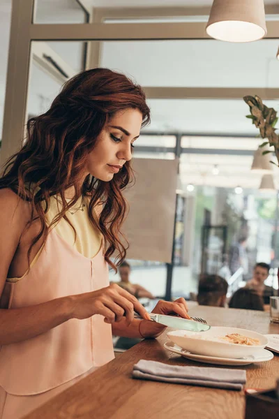 Vista lateral de la mujer joven comiendo pasta italiana en la cafetería - foto de stock
