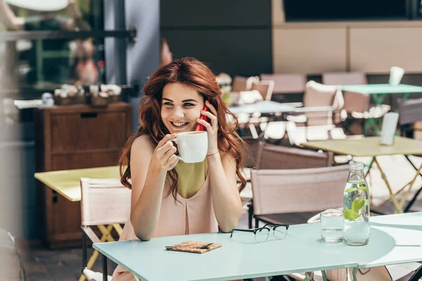 Портрет улыбающейся женщины с чашкой кофе разговаривающей по смартфону в кафе — стоковое фото