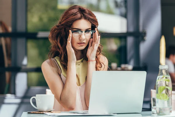 Portrait de jeune blogueur en lunettes travaillant sur ordinateur portable dans un café — Photo de stock