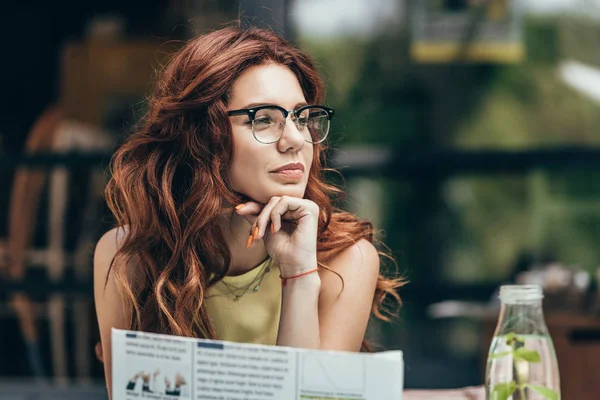 Portrait of attractive young woman in eyeglasses with newspaper in restaurant — Stock Photo