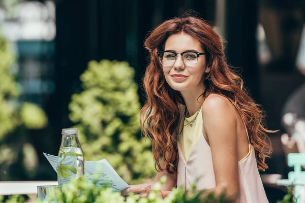 Vista lateral de atractiva joven en gafas con periódico en restaurante - foto de stock