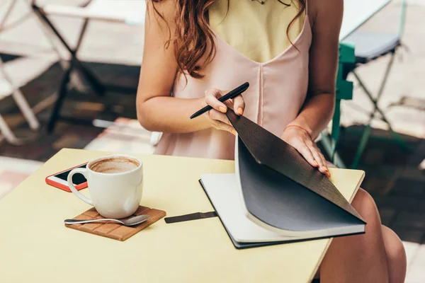 Cropped shot of businesswoman with notebook at table in cafe — Stock Photo