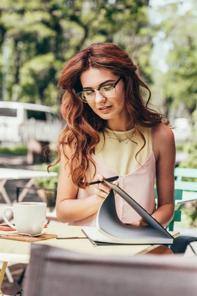 Retrato de joven mujer de negocios en gafas con cuaderno en la mesa en la cafetería - foto de stock