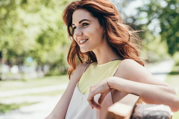 Vista laterale della giovane bella donna appoggiata sulla panchina nel parco — Foto stock