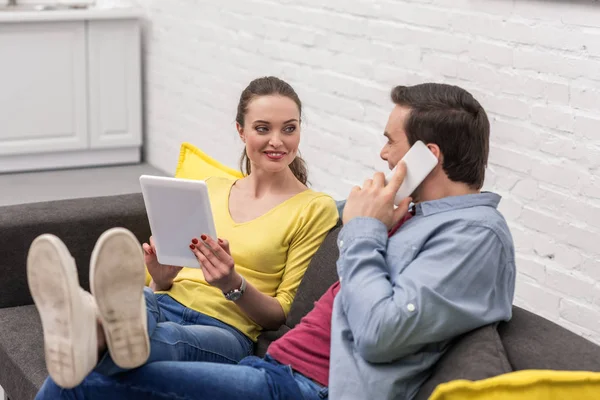 Feliz pareja de adultos relajarse en el sofá en casa y el uso de gadgets - foto de stock