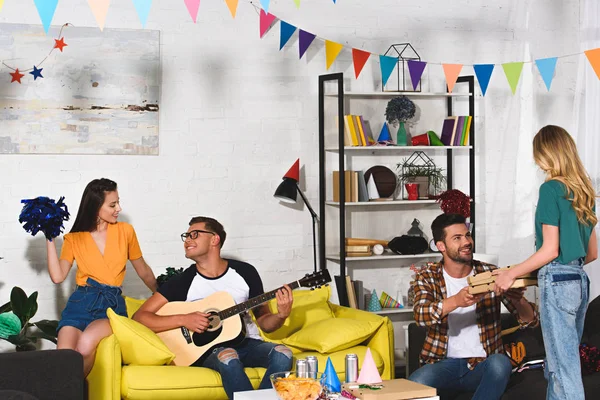 Smiling young people with pizza, beer and guitar having fun together at home party — Stock Photo