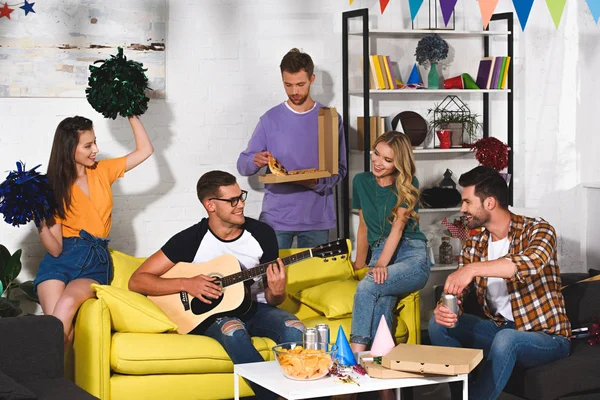 Щасливі молоді друзі з піцою, пивом і гітарою розважаються разом на домашній вечірці — стокове фото