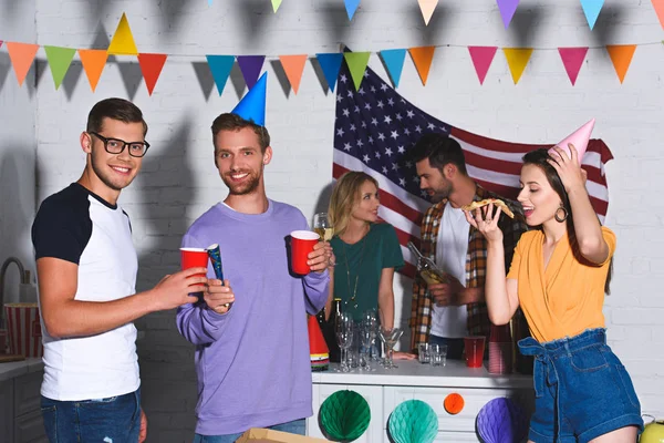 Jóvenes sonriendo a la cámara mientras beben cerveza y festejan con amigos - foto de stock