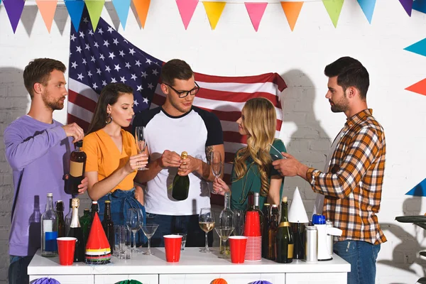 Красивые улыбающиеся молодые друзья пьют вино на домашней вечеринке — стоковое фото