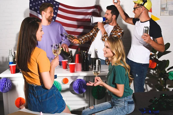 Chicas bebiendo vino y sonriendo el uno al otro mientras los hombres de fiesta detrás - foto de stock