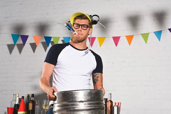 Handsome young man in beer hat holding keg of beer and smiling at camera — Stock Photo