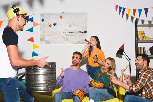 Happy young man holding beer barrel and looking at smiling friends — Stock Photo