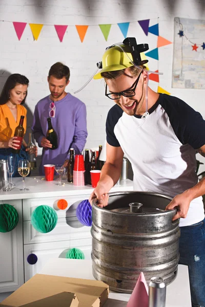 Souriant jeune homme tenant tonneau de bière tandis que les amis de boire derrière — Photo de stock