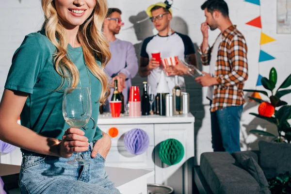 Recortado disparo de sonriente chica sosteniendo vaso de vino mientras amigos masculinos beber cerveza detrás - foto de stock