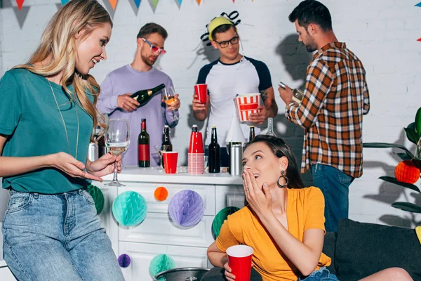 Smiling female friends drinking alcoholic beverages and talking at home party — Stock Photo