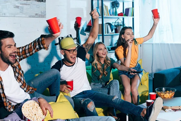 Happy young friends drinking beer and watching tv at home — Stock Photo