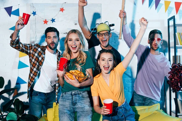 Felici giovani uomini e donne sorridenti alla fotocamera mentre si divertono insieme a casa festa — Foto stock