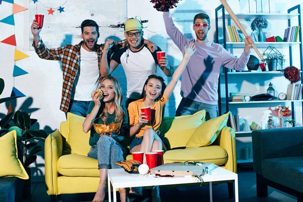 Heureux jeunes hommes et femmes amis boire de la bière et sourire à la caméra à la fête à la maison — Photo de stock