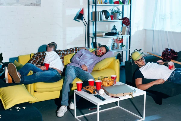Borrachos jóvenes amigos varones durmiendo en sofás después de la fiesta en casa - foto de stock