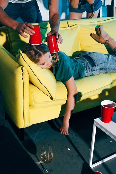Colpo ritagliato di giovane uomo in possesso di bicchieri di plastica sopra la testa di dormire ragazza ubriaca a casa festa — Foto stock