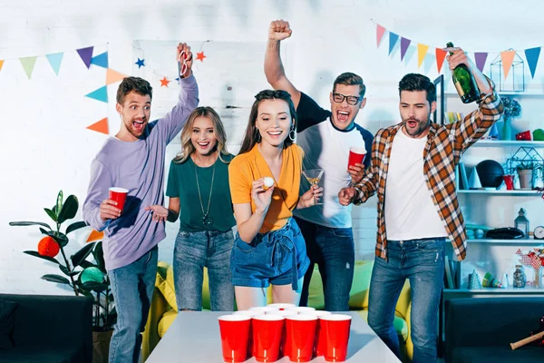 Glückliche junge Freunde schauen lächelndes Mädchen beim Bierpong auf der Heimparty an — Stockfoto